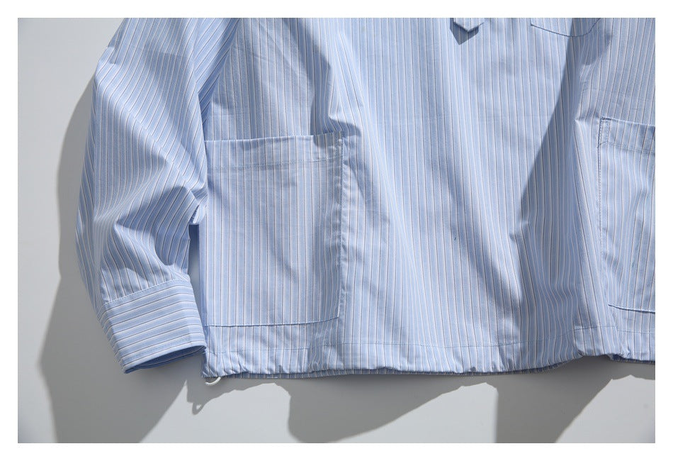 Cropped flat lay of a light blue pinstriped button-up shirt showing its front pockets, cuff and hem.
