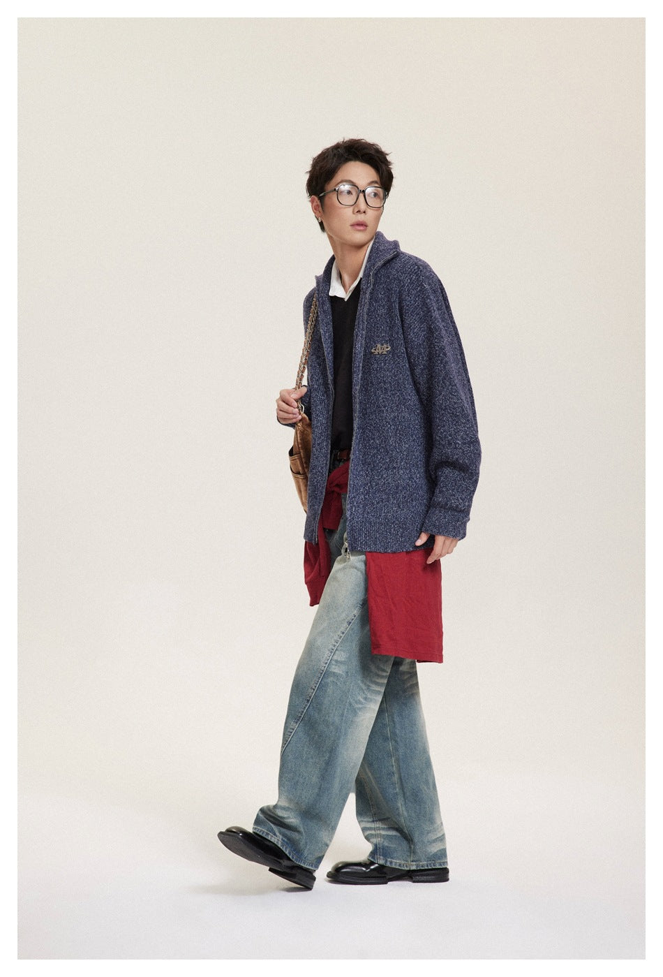 Model wearing navy knit zip sweater with stand collar, black top, red layer, light-wash jeans and brown shoulder bag