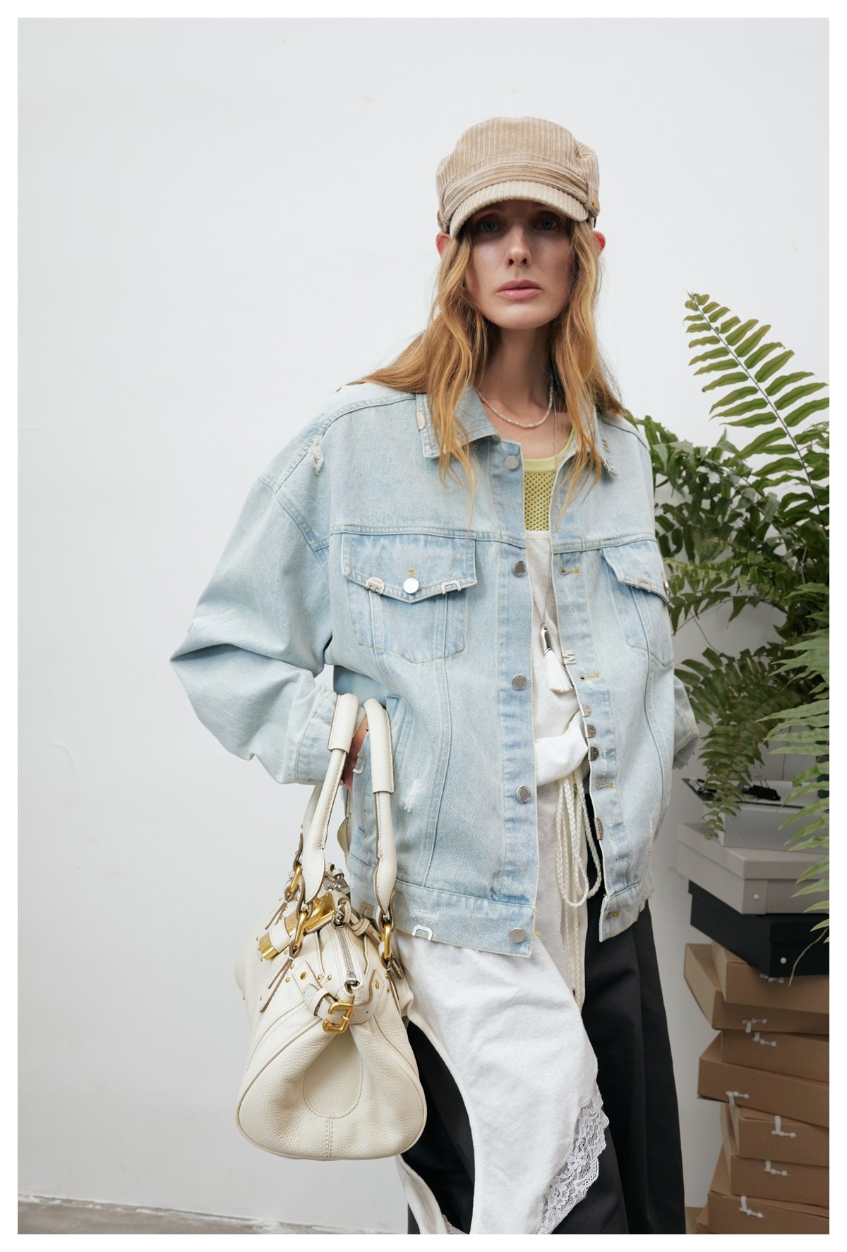 Model wearing an oversized light-wash denim jacket with distressed details, flap pockets and metal accents.