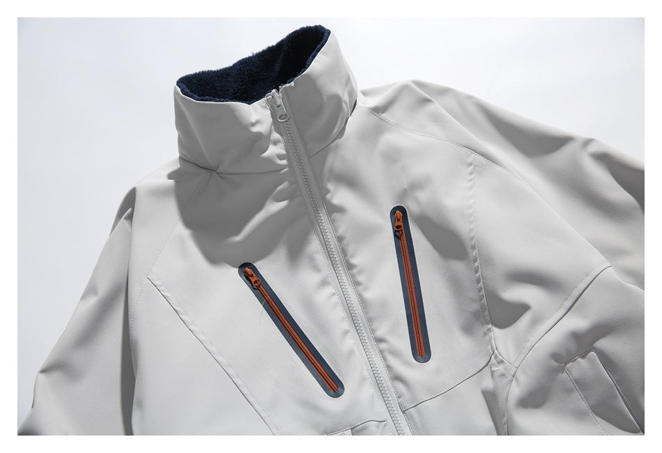 Close-up of a light gray jacket showing its high collar, center zipper and two orange-trimmed chest zippers.