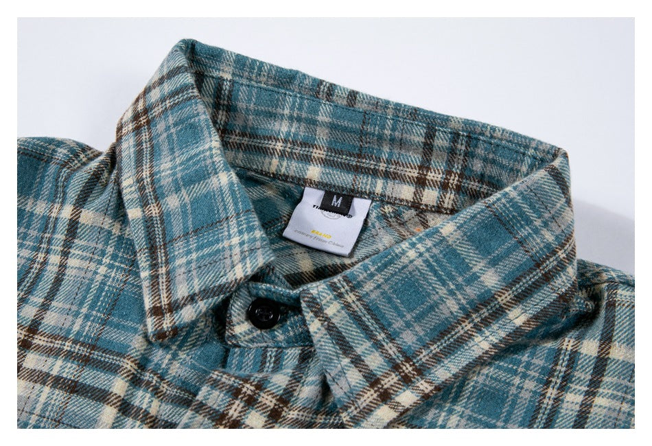 Close-up of a blue, cream, and brown plaid shirt collar with a black button and visible size tag.