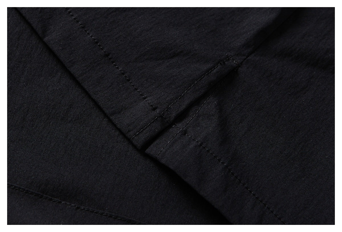 Close-up of black garment fabric with intersecting stitched seams and overlapping panels.