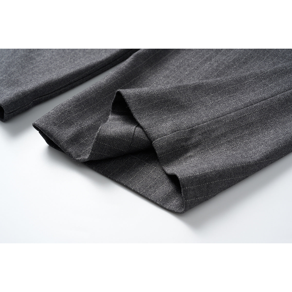 Close-up of the wide trouser hems, showing the dark charcoal pinstripe fabric and stitched hem.