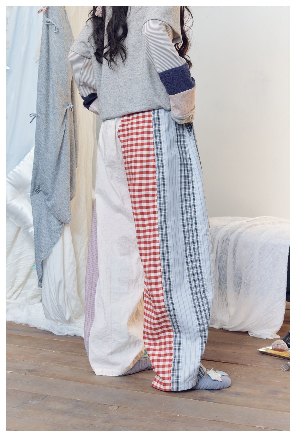 Back view of a model wearing wide patchwork trousers with red gingham, blue stripes, lilac checks and white panels.