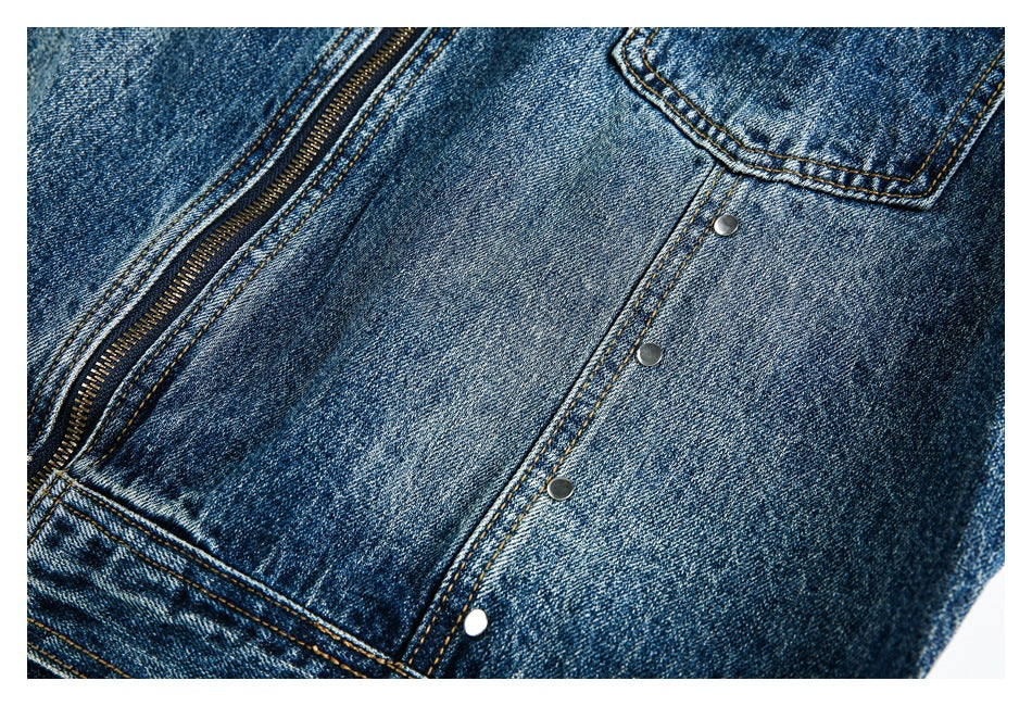Close-up of a blue denim garment showing a metal zipper, pocket edge and line of snaps.