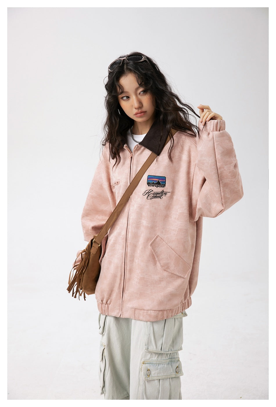 Closer view of the dusty pink jacket's dark collar, zip closure, chest embroidery, and front pocket.