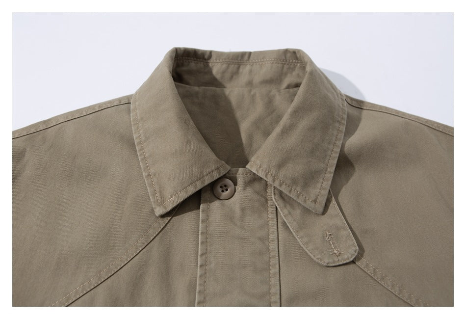 Close-up of a taupe jacket collar and button fastening, with a small stitched motif on the collar tab.