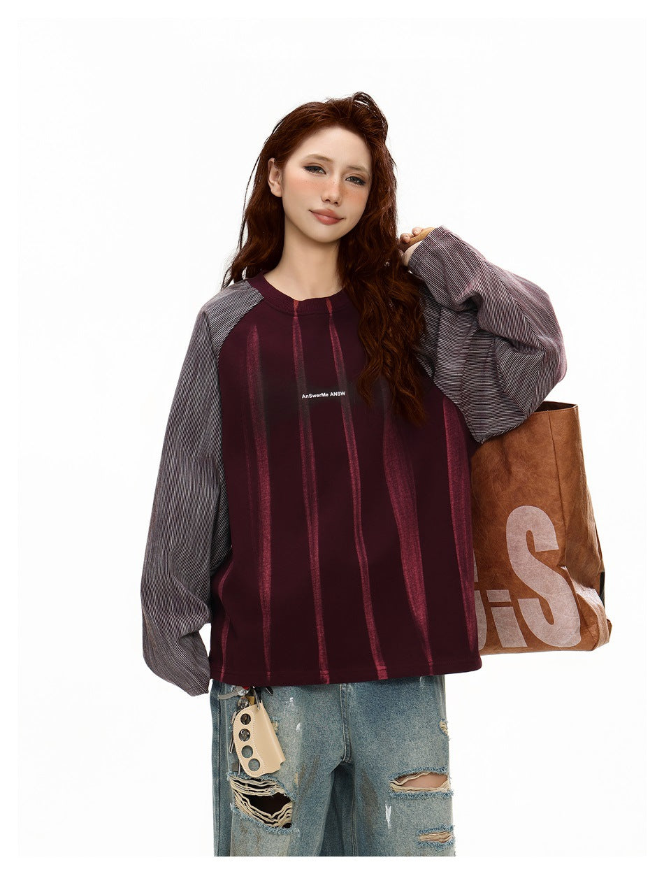 Model wearing a burgundy vertically striped top with gray pinstriped raglan sleeves and distressed jeans.