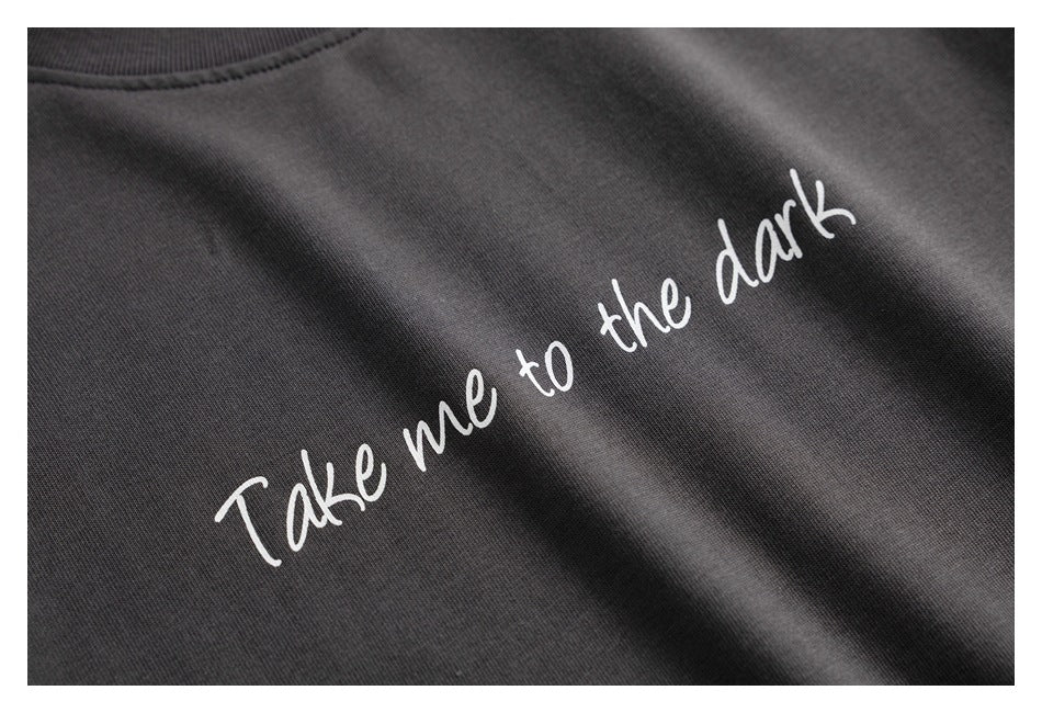 Close-up of white script reading “Take me to the dark” printed on charcoal T-shirt fabric.