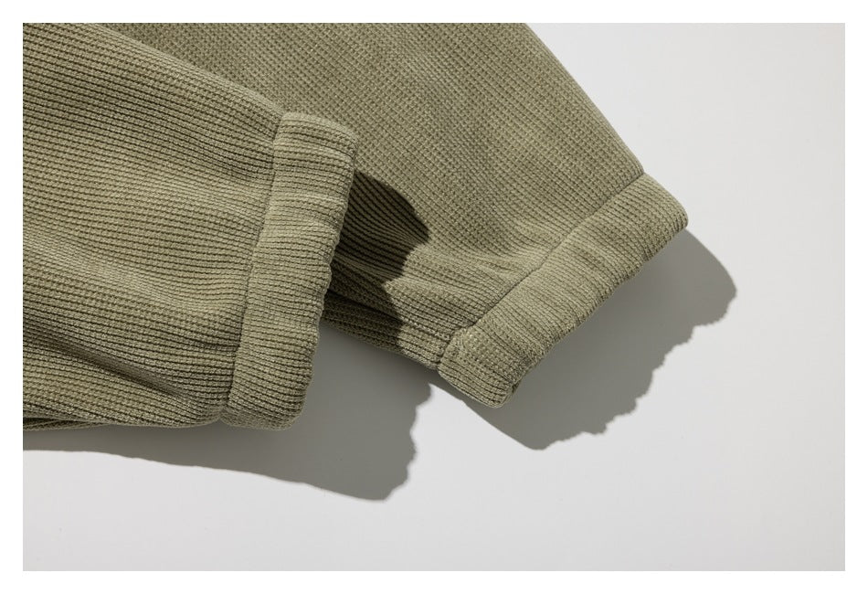 Close-up of olive ribbed garment edges with a folded cuff or hem on a white surface.