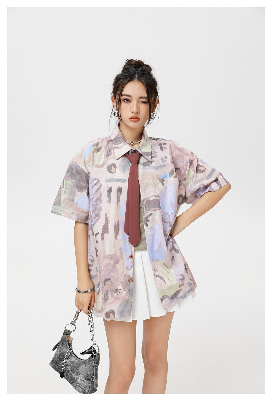 Model wearing a pastel abstract-print short-sleeve button-up shirt with a chest pocket, burgundy tie and white skirt.