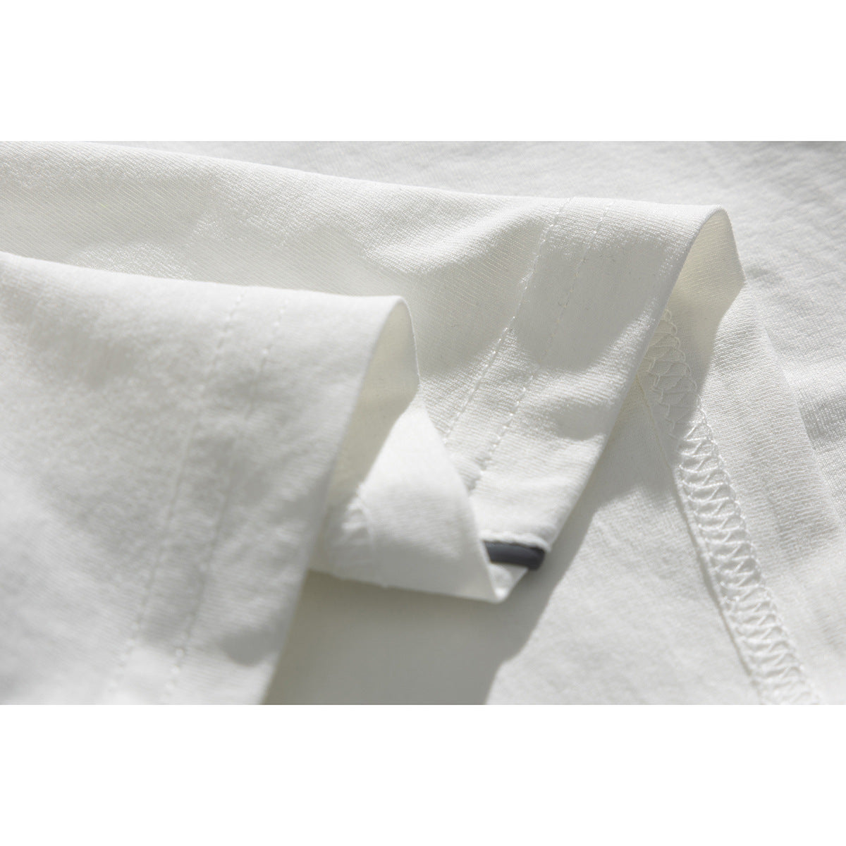 Close-up of white T-shirt fabric showing a folded sleeve edge and overlocked seam.