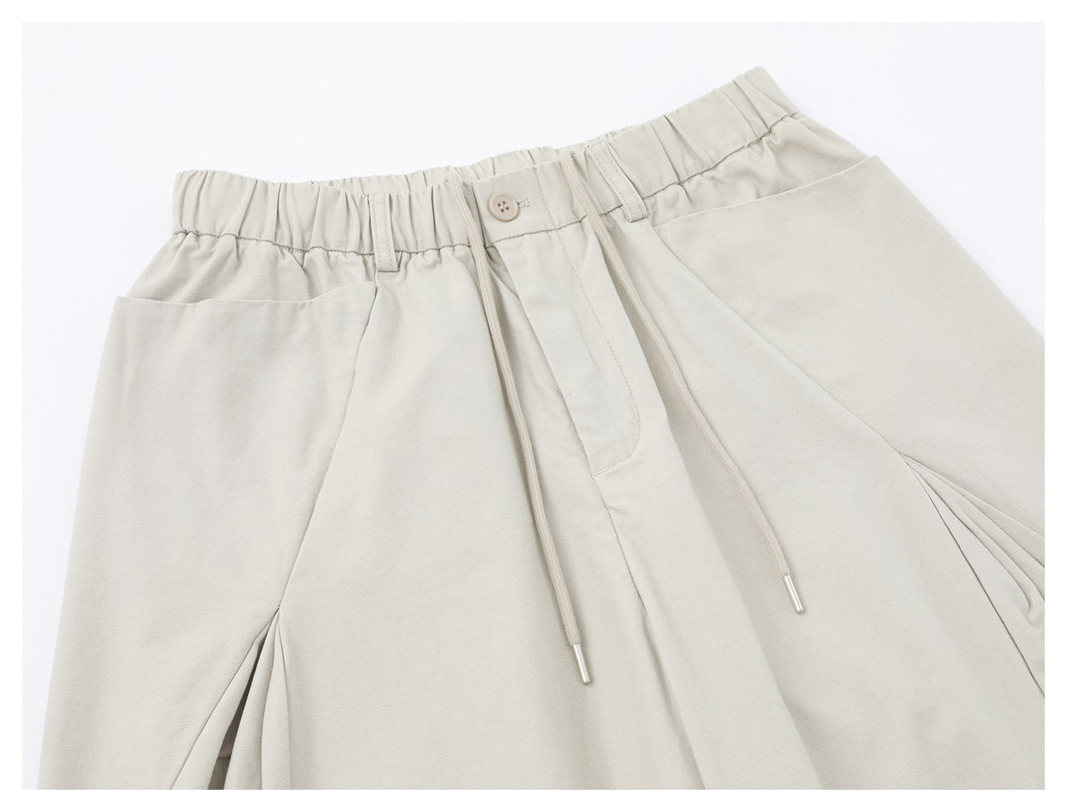 Close-up of light ivory trousers showing the elastic waist, button, drawstrings, belt loops and front pleats.