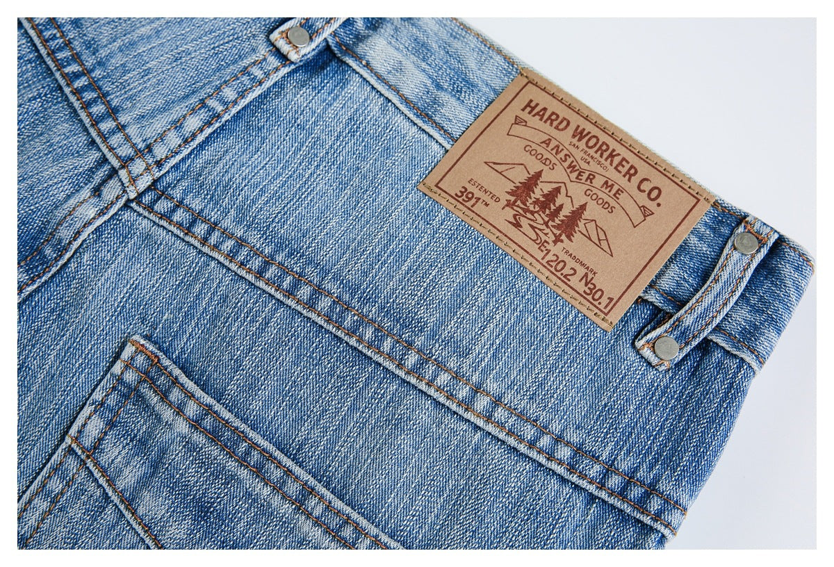 Close-up of a tan leather brand patch and metal rivets on the waistband of faded blue jeans.