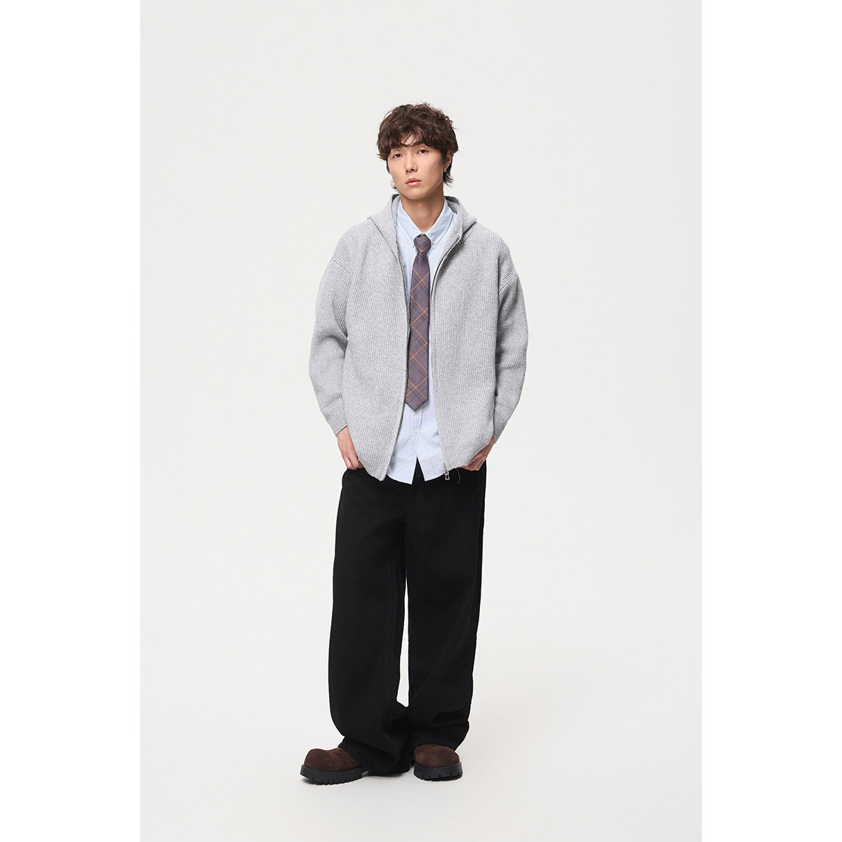 Model wearing a light gray zip-front hooded sweater over a striped shirt and tie, with black wide-leg trousers.