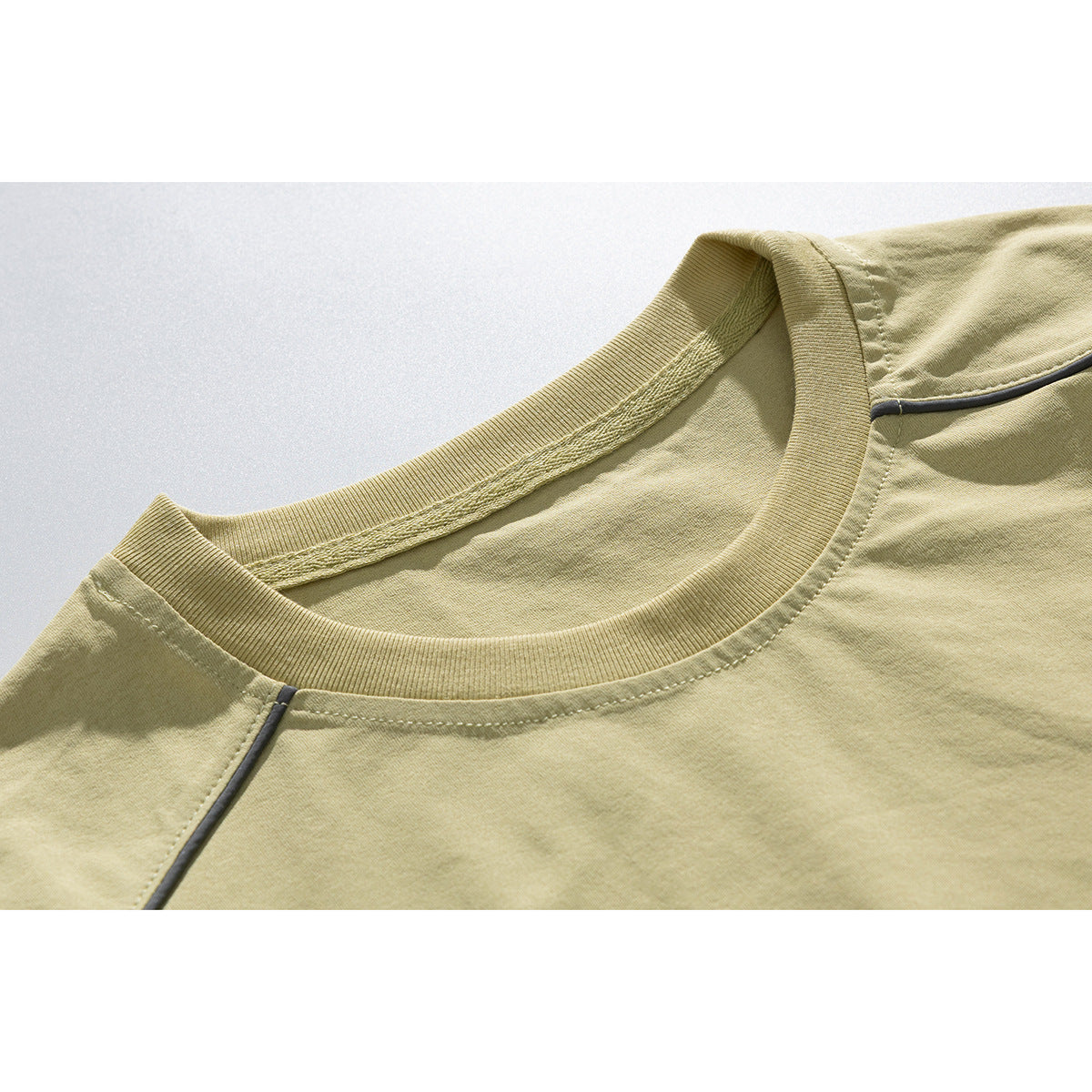 Close-up of a pale khaki T-shirt's ribbed crew neck and dark piping along the raglan seam.