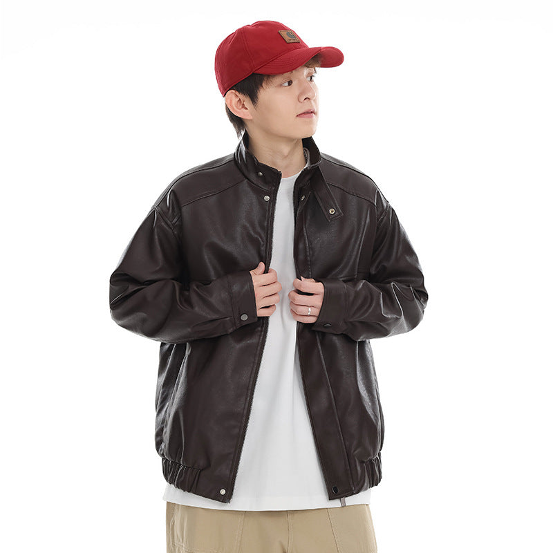 Model wearing a dark brown stand-collar jacket with snap details and an elastic hem, over a white shirt and beige trousers.