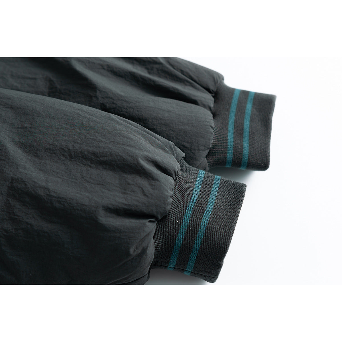 Close-up of black jacket sleeves ending in ribbed cuffs with teal stripes.