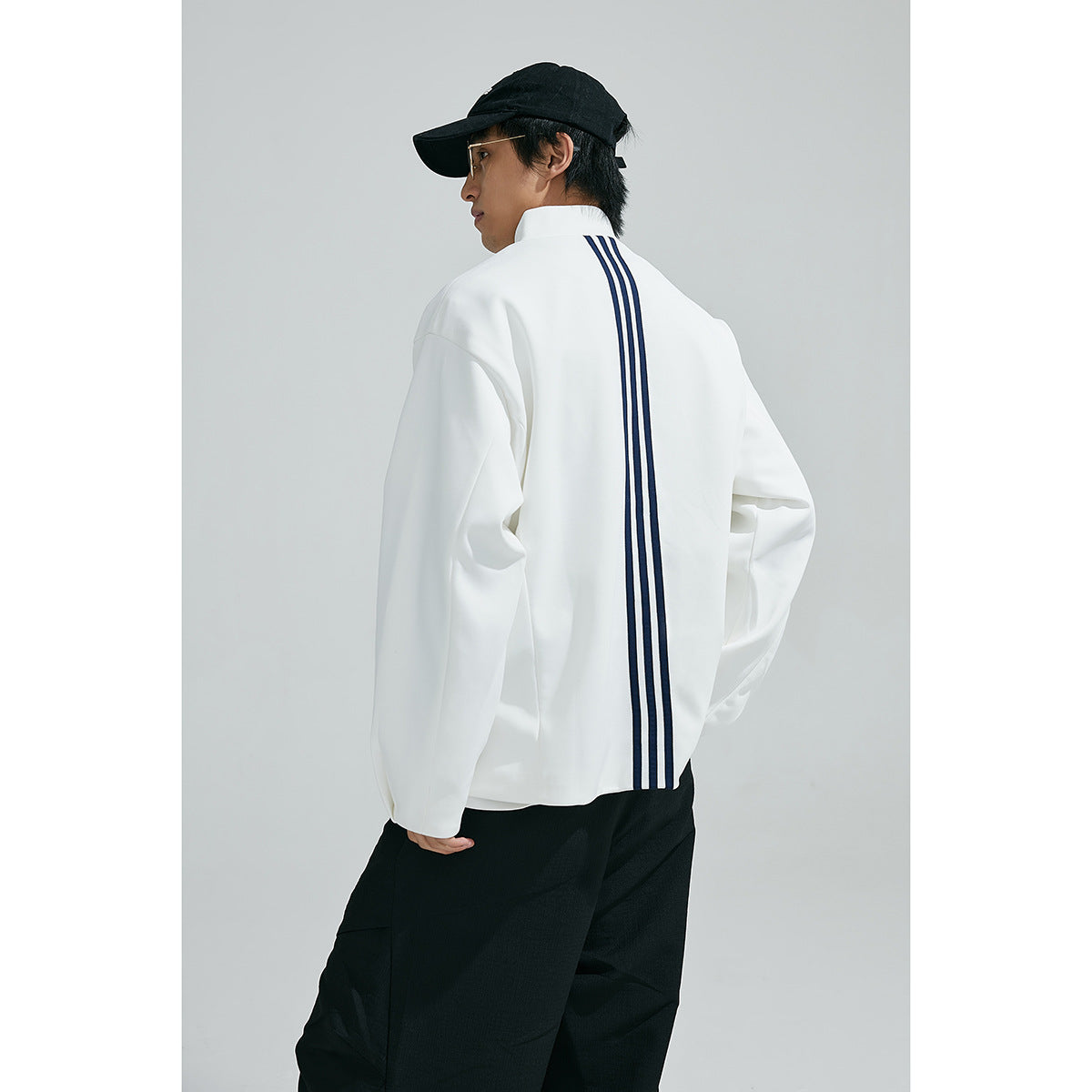 Rear view of a model wearing a white jacket with three dark vertical stripes down the back.