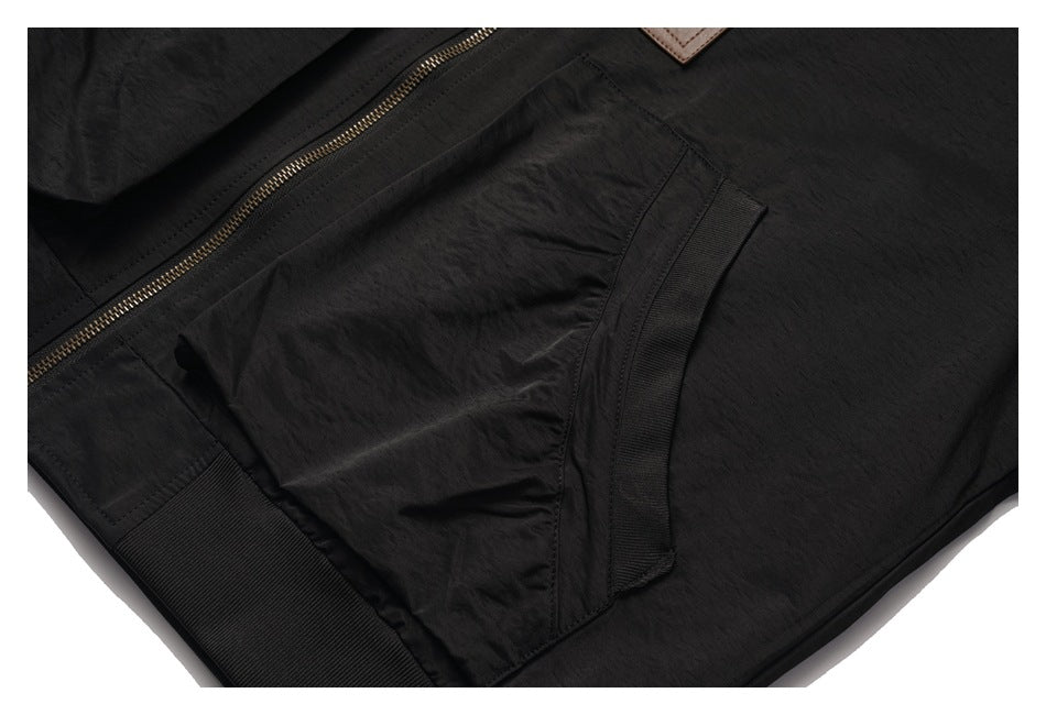 Close-up of a black jacket pocket and ribbed trim beside the brass-tone front zipper.