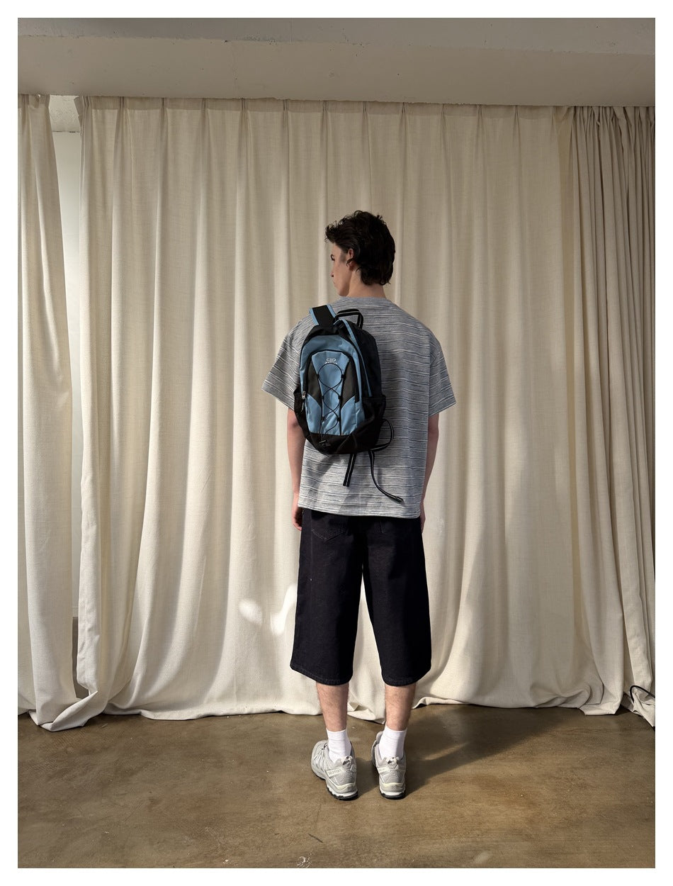 Rear view of a model wearing a gray striped T-shirt and black knee-length shorts with a blue-and-black backpack.