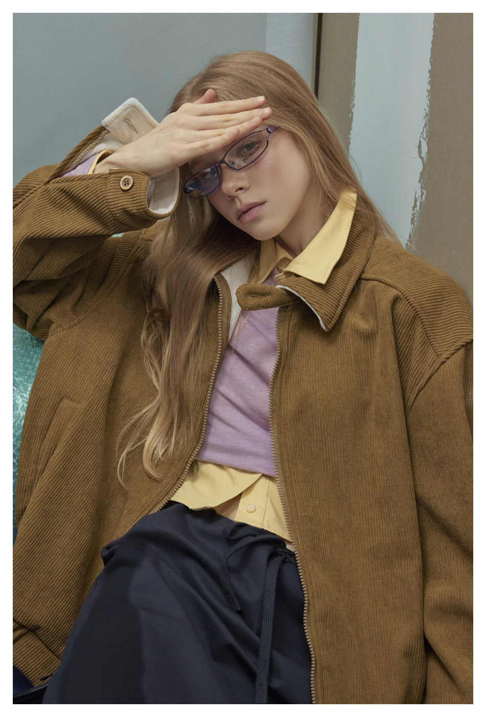 Close view of a model wearing a brown ribbed jacket, showing its wide collar, zipper, and sleeve button.