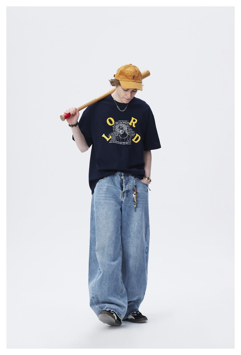 Model wears a navy oversized graphic T-shirt with blue wide-leg jeans and a mustard cap.