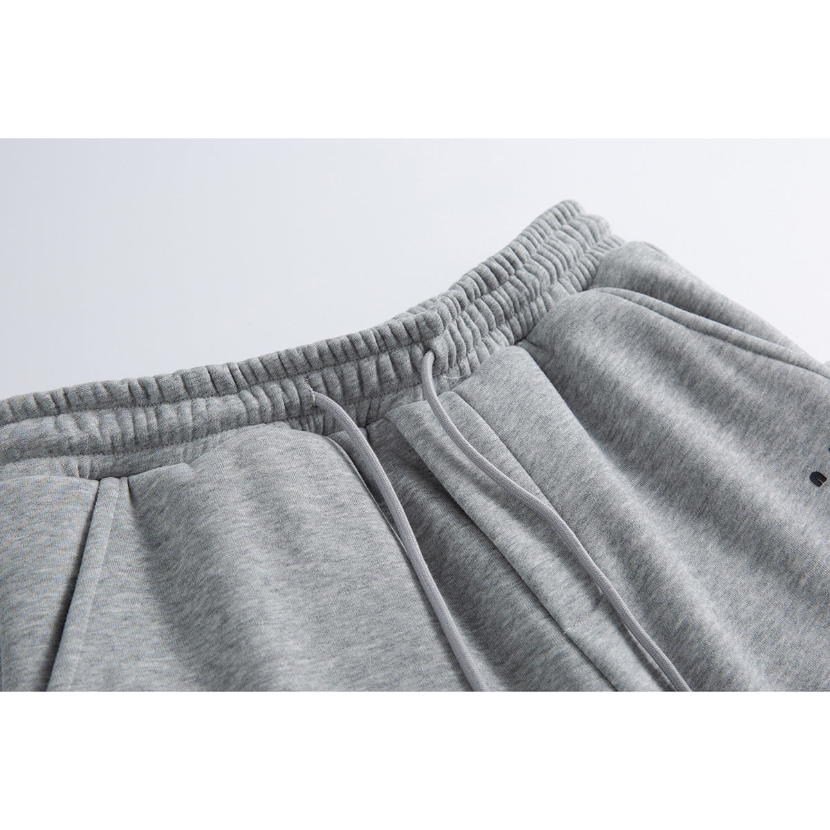Close-up of heather-gray pants showing the elastic waistband, drawstrings, and front seams.