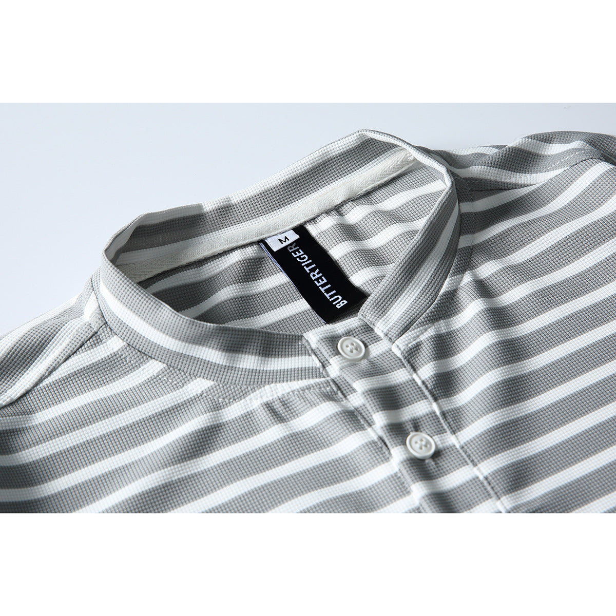 Close-up of a gray-and-white striped shirt with a band collar, white buttons, and a black neck label.