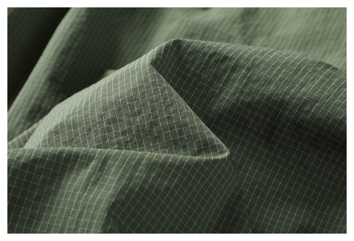 Macro view of olive green fabric with a fine white grid pattern and softly folded texture.