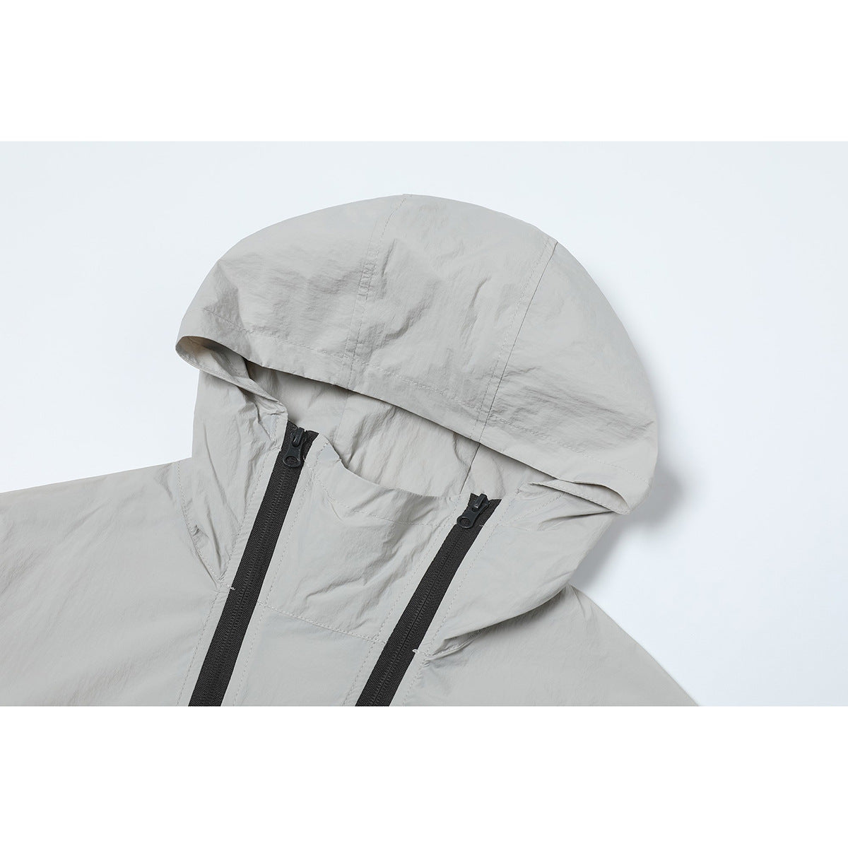 Close-up of a light gray hooded jacket showing the hood, high collar, and two black zippers.