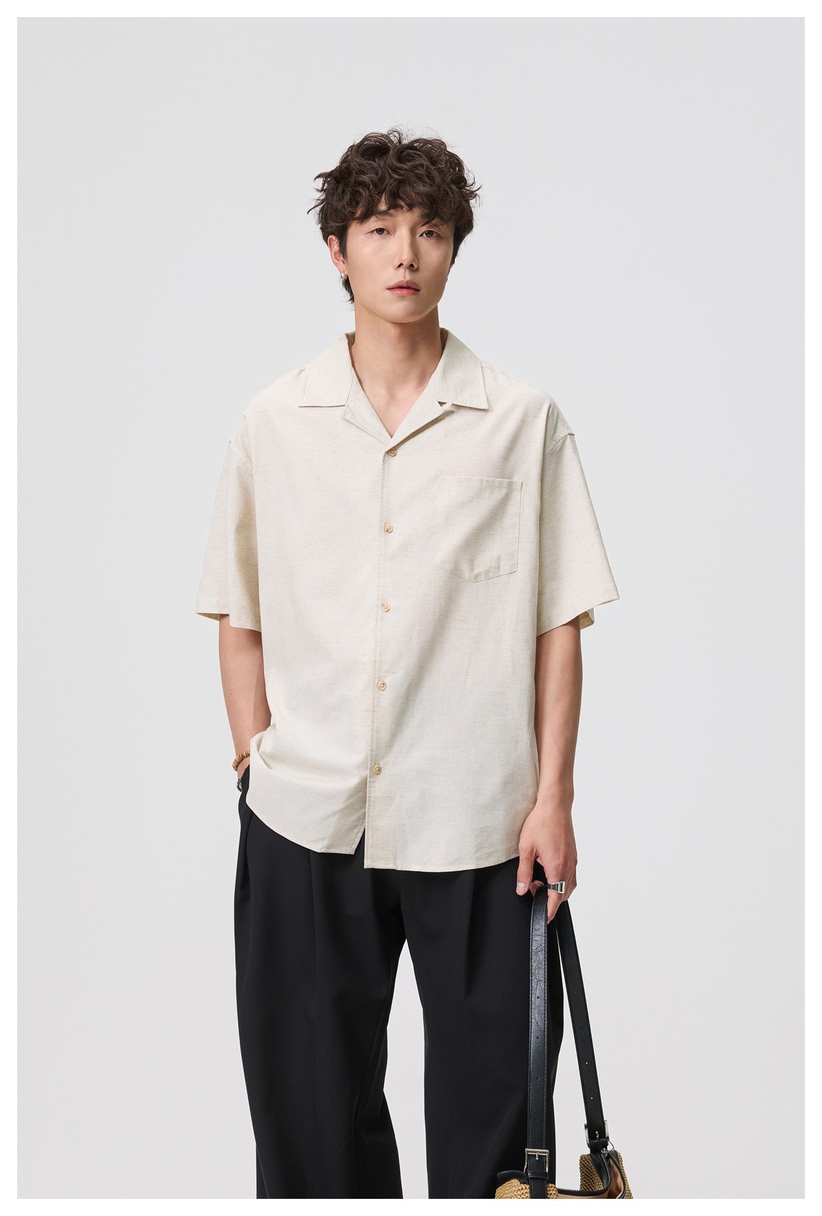 Male model wearing an off-white short-sleeve button-up shirt with an open collar and chest pocket, paired with black