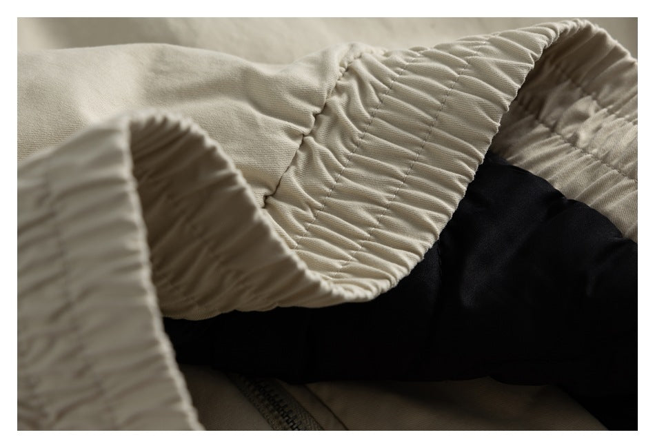 Close-up of a beige garment's gathered elastic cuff beside black fabric and a zipper.