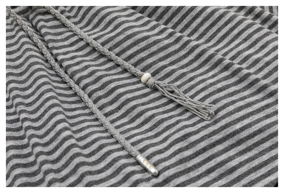 Close-up of braided drawstrings on a gray-and-charcoal striped garment, with a white bead and metal-colored tips.