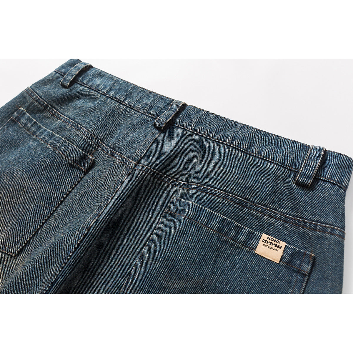 Close-up of the back waist and pockets of blue distressed jeans, with a small beige label.
