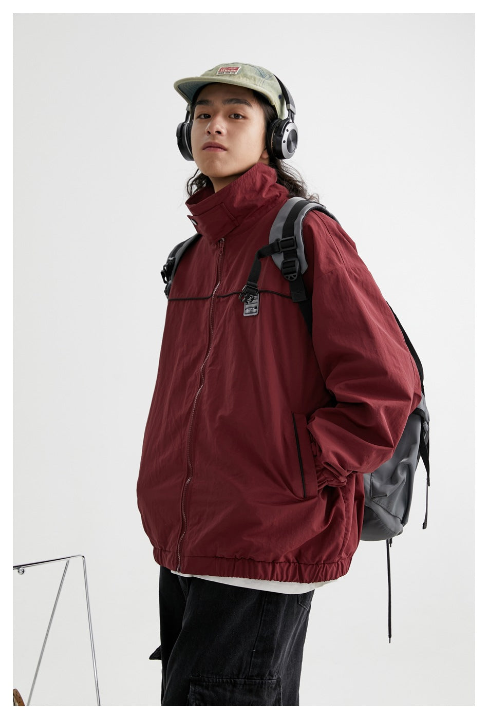 Closer view of a model wearing a burgundy jacket with a high stand collar, front zipper, black piping and side pockets.