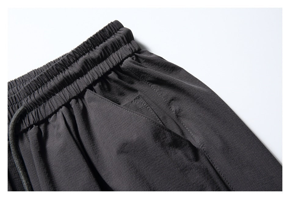 Close-up of charcoal pants showing the gathered elastic waistband and angled front pocket.
