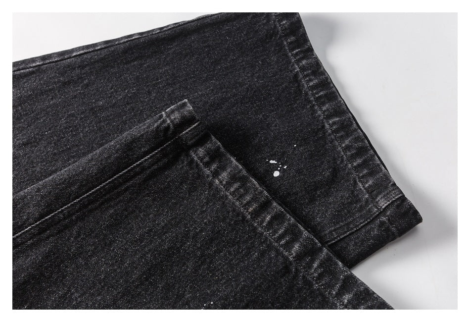 Close-up of black denim trouser hems with visible stitching and small white paint-like specks.