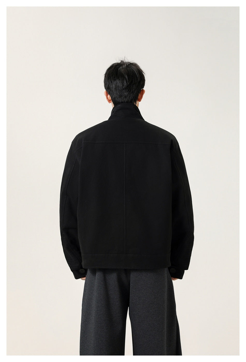 Back view of a model wearing a black jacket with a high collar and center-back seam.