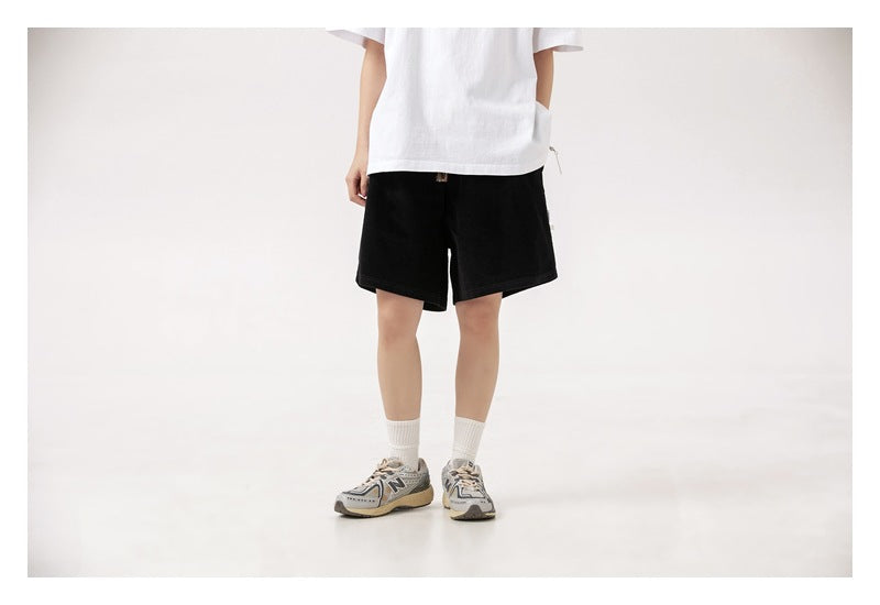 Front view of a model wearing loose black shorts with a white T-shirt.