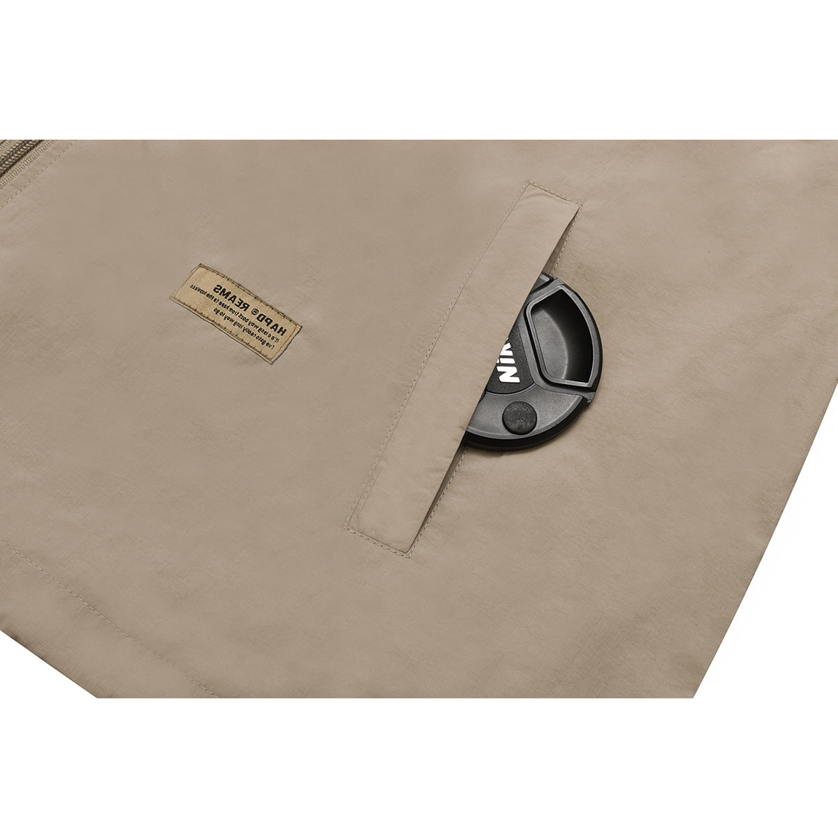 Close-up of a beige jacket pocket with a flap and a small sewn text label.