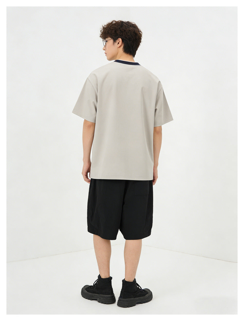 Rear view of a model wearing a light gray short-sleeve T-shirt with a dark collar and black shorts.