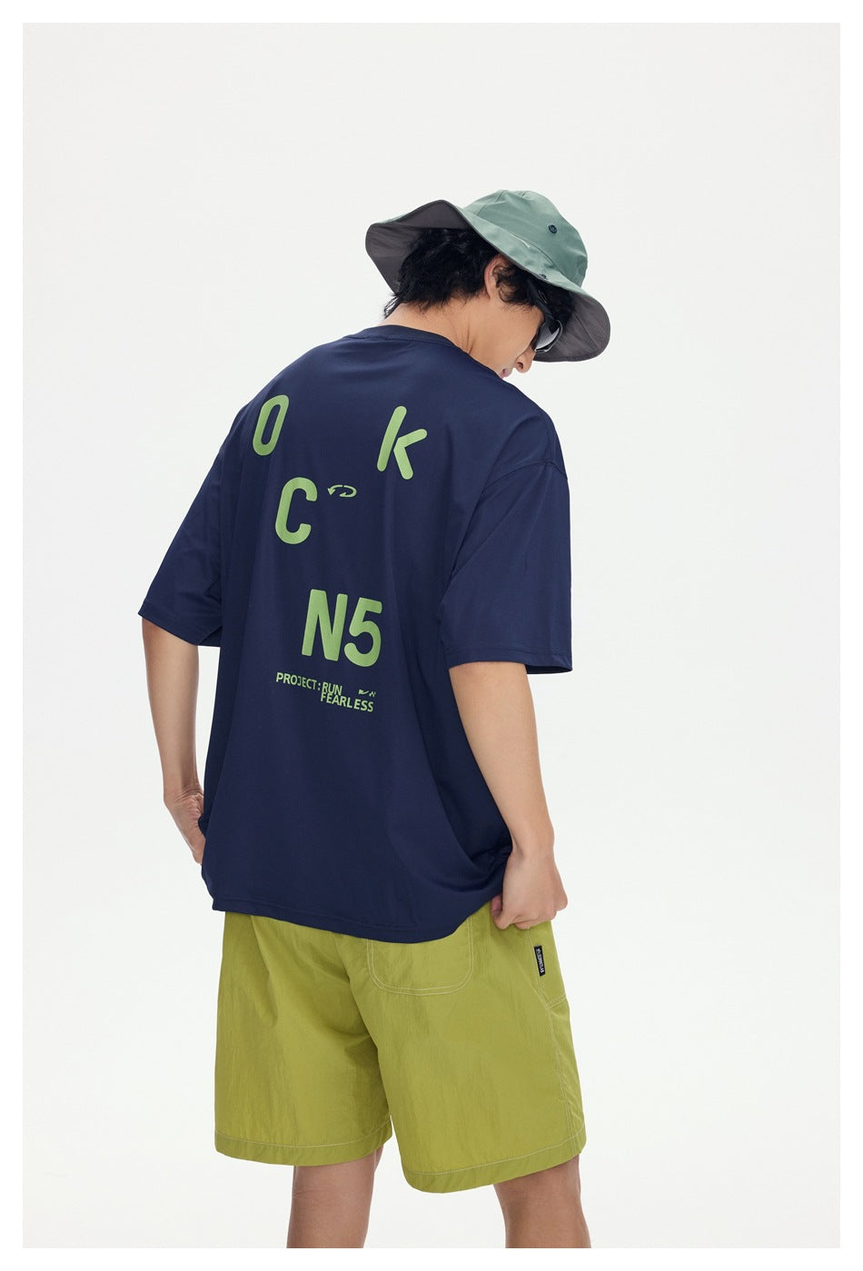 Three-quarter back view of a model showing the lime graphic print on a navy T-shirt and lime shorts.