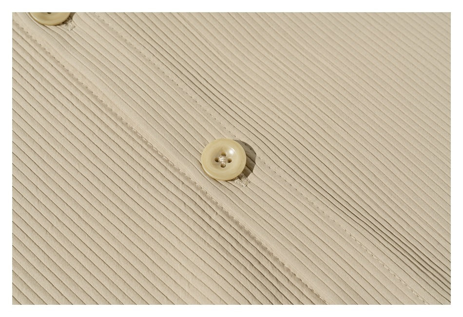 Close-up of a beige button and stitched placket against the shirt's fine ribbed surface.