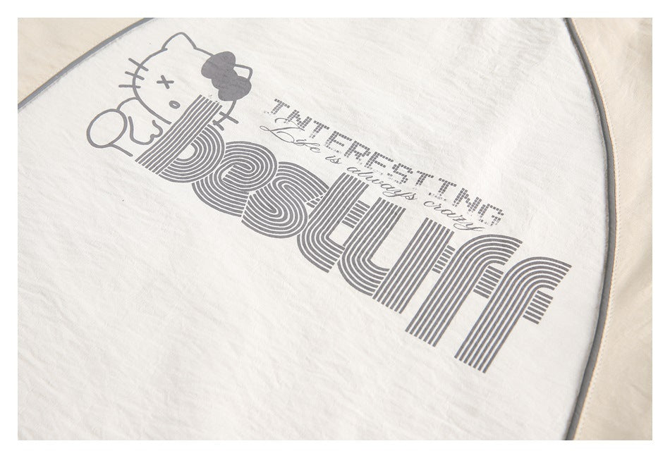 Close-up of a cream top with a gray cartoon cat and large striped lettering printed on the front.