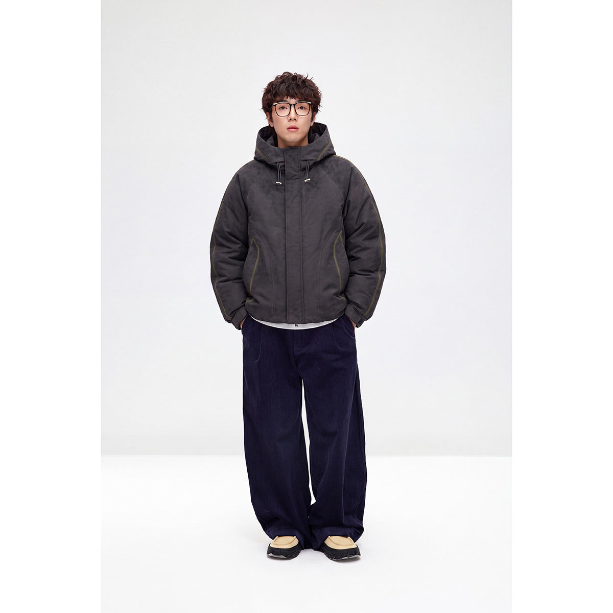 Full-length model wearing a charcoal hooded jacket with front pockets and a concealed-looking front closure.