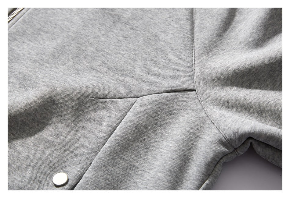 Close-up of a heather gray jacket showing a seam, metal snap, and edge of the zipper.