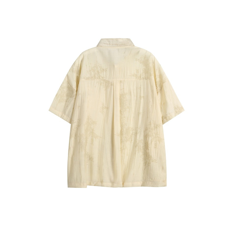Back view of a loose ivory short-sleeve collared shirt with a subtle pale botanical pattern.