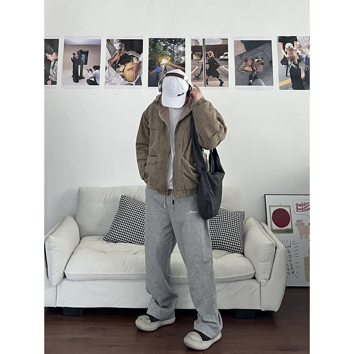 Person wearing an olive-brown hooded jacket with front pockets, gray sweatpants, and a white cap, shown from the front.