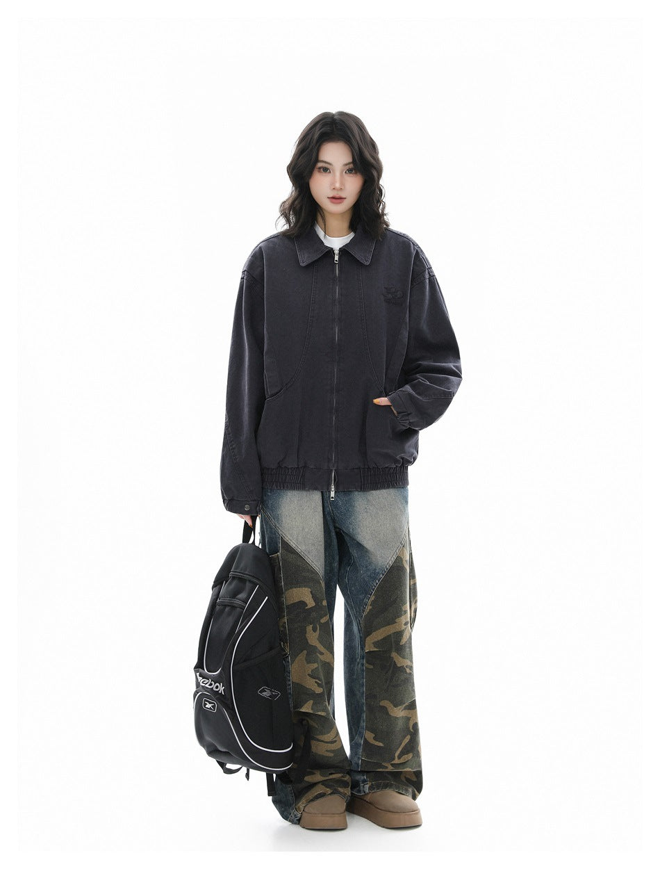 Full-length model wearing a charcoal zip-front jacket with a pointed collar and gathered hem, paired with patchwork pants.